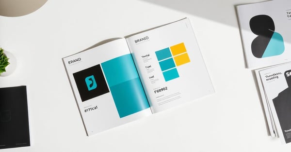 An open brand guidelines booklet showing logo, type and color rules beside printed stationery